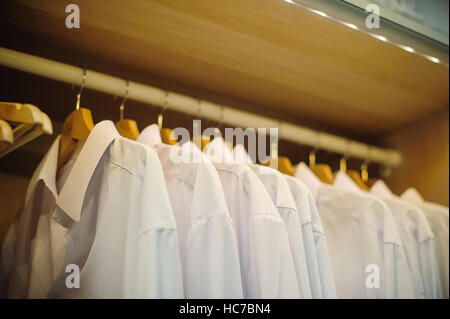 Weiß mans Hemden auf Kleiderbügeln im store Stockfoto