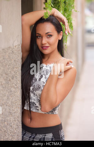 Hübsche junge Frau mit langen dunklen Haaren in Sport/Freizeit-Outfit, im Freien. Stockfoto
