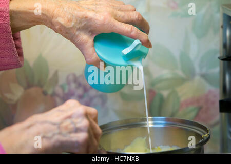 Ältere Frau gießt Milch in Topf auf Herd-Victoria, British Columbia, Kanada. Stockfoto