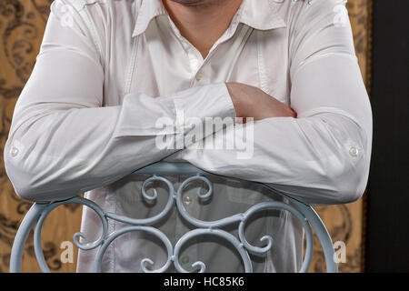 männliche Hände in einem weißen Hemd gefaltet auf seiner Brust Closeup auf Rückseite der weißen Stuhl Stockfoto