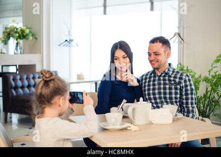 Familie, Elternschaft, Menschen Technologiekonzept - Nahaufnahme von glückliche Mutter, Vater und kleine Mädchen essen, Kind nehmen Foto per Smartphone im Restaurant Stockfoto