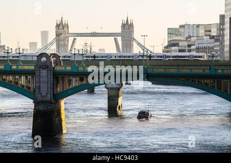 Schmales Boot auf der Themse in London unter Brücken. Ein winterlicher, nebeliger Blick am Morgen über die Southwark Bridge in Richtung Tower Bridge Stockfoto