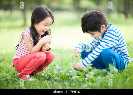 Seitliche Ansicht des lächelnden jungen und Mädchen sitzen und berühren Pflanzen in Feld Stockfoto