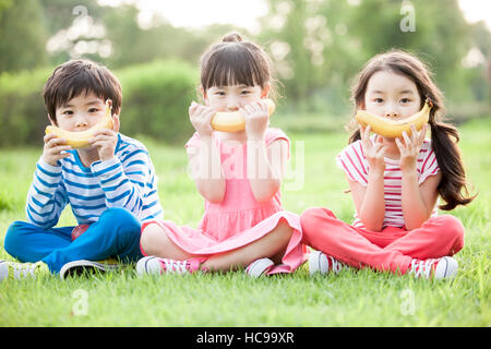 Drei lachende Kinder mit Bananen sitzen auf Feld Stockfoto