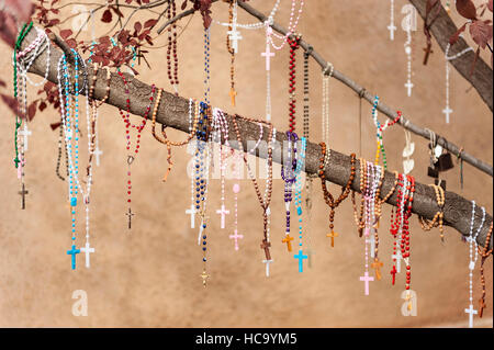 Verschiedene Rosenkränze / Gebete hängen von einem Ast an El Santuario de Chimayó, eine römisch-katholische Kirche in Chimayó, New Mexico Stockfoto