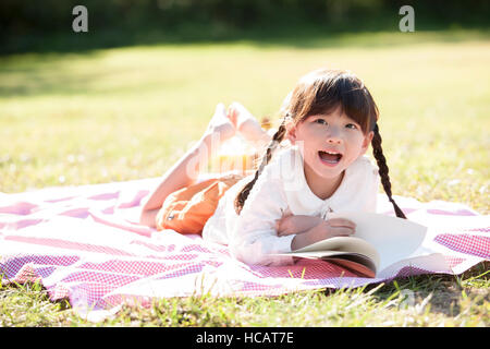 Lächelnde Mädchen verdeckt liegend ein Buch nachschlagen bei Picknick Stockfoto
