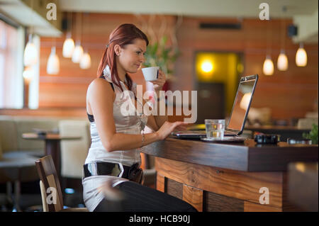 Junge Frau in einem Kaffeehaus an der Theke sitzen an einem Notebook arbeitet Stockfoto