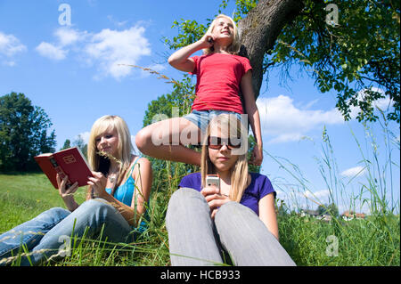 Drei Mädchen im Teenageralter mit Handys und einem Buch auf Wiese Stockfoto