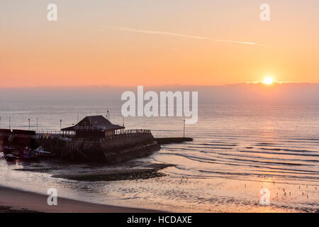 Helle Sonnenaufgang erscheinen über eine Schicht von Wolke am Horizont mit hellen orange Himmel oben. Vordergrund Broadstairs Hafen und Strand. Ruhiges Meer. Stockfoto