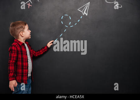 Niedlicher kleine Junge gekleidet im Hemd in einem Käfig betrachten Pfeil gezeichnet auf Tafel und deutete darauf. Stockfoto