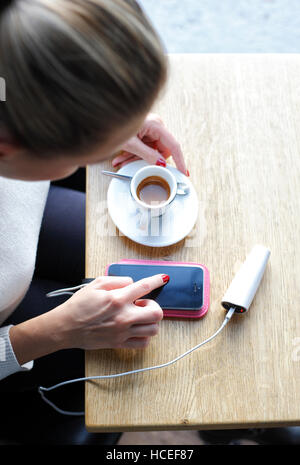 Frau Handy laden und Café-Bar eintippen Stockfoto