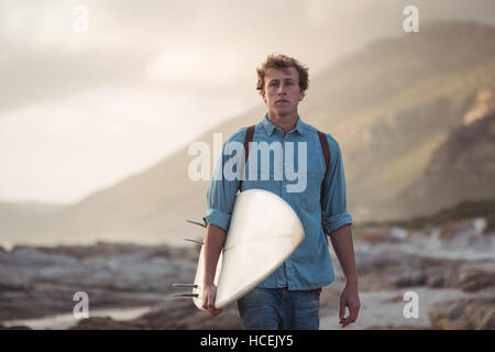 Mann trägt ein Surfbrett zu Fuß auf dem Seeweg Stockfoto