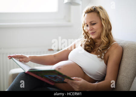 Schöne schwangere Frau Buch auf sofa Stockfoto