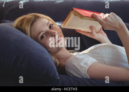 Portrait der schönen Frau liegend auf Sofa und Lesebuch im Wohnzimmer Stockfoto