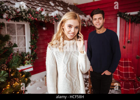 Junges Paar in Pullover neben dem roten Haus. Mann im Hintergrund Stockfoto