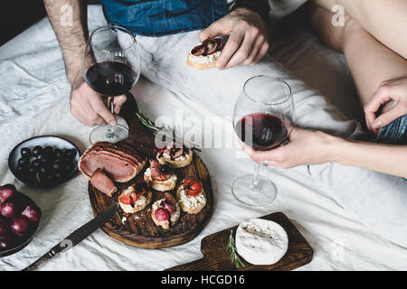 Paar beim Abendessen mit Rotwein und Antipasti snacks Satz: Bruschetta, Crostini, geheilt Fleisch, Oliven, Käse und Wein Stockfoto