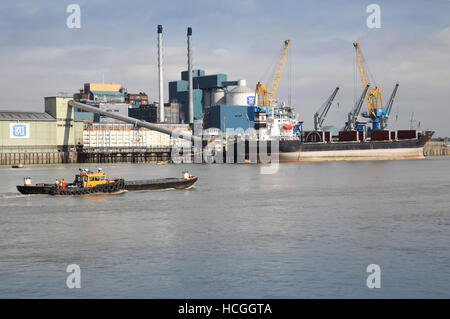 Ein Lastkahn übergibt die Tate and Lyle Zuckerraffinerie neben der Themse bei Silvertown in Londons Docklands. Zeigt Schiff vor Anker. Stockfoto