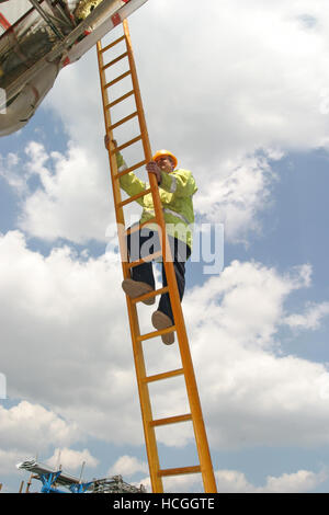 Ein Bauarbeiter klettert eine Langholz-Pol-Leiter. Von unten fotografiert mit blau, bewölkten Himmel im Hintergrund. Stockfoto