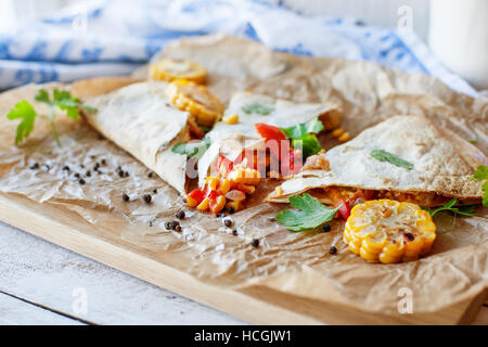 Mexikanisches Quesadilla Wrap mit Gemüse, Mais, Paprika und Saucen auf Pergament und Tisch. horizontale Ansicht. Stockfoto