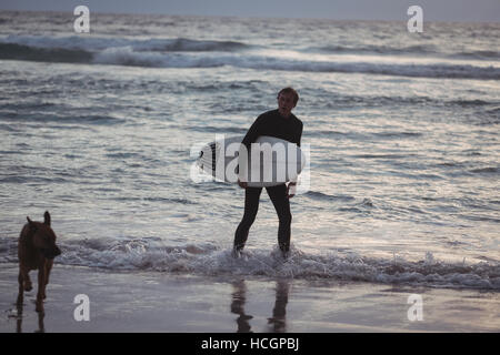 Mann mit Surfbrett stehend mit seinem Hund am Strand Stockfoto