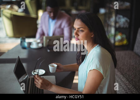 Nachdenklich Geschäftsfrau halten Kaffeetasse sitzt an ihrem Schreibtisch Stockfoto