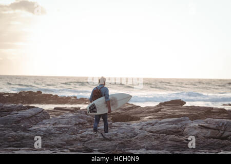 Mann trägt ein Surfbrett zu Fuß auf dem Seeweg Stockfoto