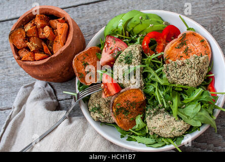 Rucola, vegane Linsensuppe gebratene Schnitzel, gebackene Süßkartoffeln, Tomaten, Avocado, Pfeffer. Gebackene Süßkartoffel mit Kräutern der Provence in einem Topf auf einem Woode Scheiben Stockfoto