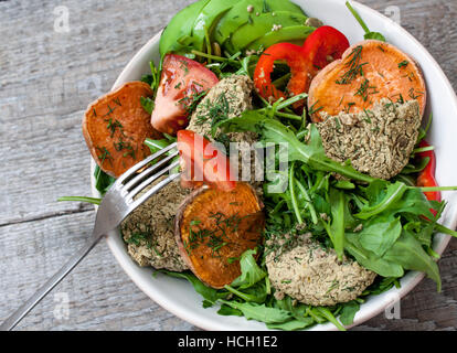 Rucola, vegane Linsensuppe gebratene Schnitzel, gebackene Süßkartoffeln, Tomaten, Avocado, Pfeffer. Gebackene Süßkartoffel mit Kräutern der Provence in einem Topf auf einem Woode Scheiben Stockfoto