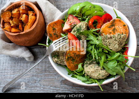 Rucola, vegane Linsensuppe gebratene Schnitzel, gebackene Süßkartoffeln, Tomaten, Avocado, Pfeffer. Gebackene Süßkartoffel mit Kräutern der Provence in einem Topf auf einem Woode Scheiben Stockfoto