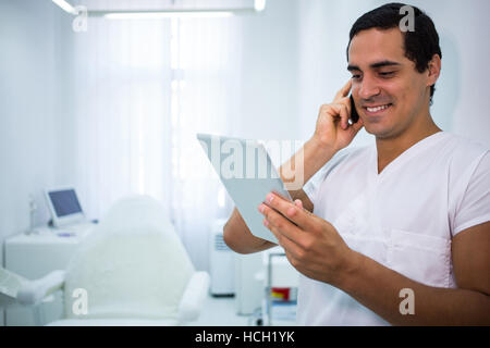 Arzt hält eine digitale-Tablette während des Gesprächs auf dem Handy Stockfoto