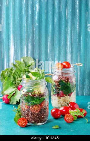 Salate mit Quinoa, Couscous, Spinat, Radieschen, Tomaten und Zucchini im Glas Einweckgläser, überragt mit frischem Gemüse aus Holz hell Türkis Stockfoto