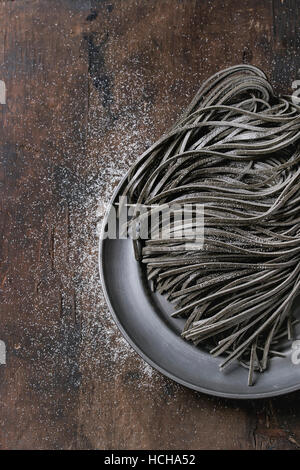 Rohe ungekochte schwarzen Tintenfisch Tinte Spaghetti Nudeln mit Mehl auf Vintage Metallplatte über dunklem Holz. Draufsicht mit Platz für Text. Stockfoto