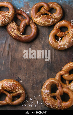 Traditionelles Bier Snack gesalzen Brezeln mit Meer-Salz und Sesam-Samen über alten dunklen hölzernen Hintergrund. Draufsicht mit Platz für Text. Oktoberfest-Thema Stockfoto