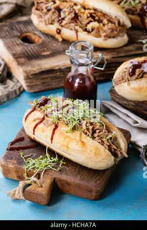 Vielzahl von pulled Pork Sandwiches mit Fleisch, gebratenen Zwiebeln, grünen Sprossen und Bbq Ketchup serviert auf Holz Schneidebrett mit kleinen Flasche Tomaten sauc Stockfoto