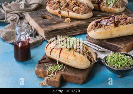 Vielzahl von pulled Pork Sandwiches mit Fleisch, gebratenen Zwiebeln, grünen Sprossen und Bbq Ketchup serviert auf Holz Schneidebrett mit kleinen Flasche Tomaten sauc Stockfoto