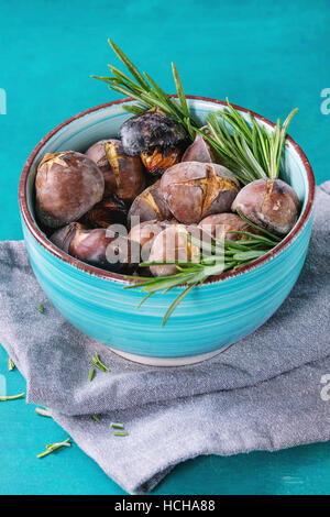 Gebratene Kastanien in der Asche mit Rosmarin in Türkis Keramikschale auf Textile Serviette über hellen blauen hölzernen Hintergrund. Stockfoto
