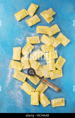 Frisch markiert rohe italienische Teigwaren-Ravioli mit Mehl und Vintage Nudeln Cutter über hellen blauen hölzernen Hintergrund. Draufsicht mit Textfreiraum. Stockfoto