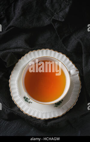 Weiße Vintage Tasse heißen Tee Untertasse steht auf schwarze Textilien Serviette über schwarze Schiefer Textur Hintergrund. Ansicht von oben Platz für text Stockfoto