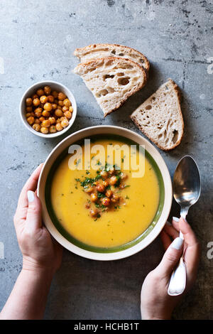 Weibliche Hände hält eine Schale mit Kürbis und gerösteten Kichererbsen-Suppe. Ansicht von oben Stockfoto