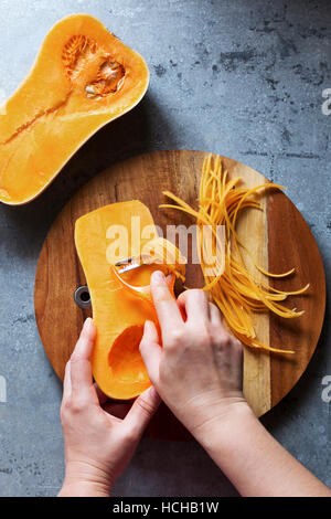 Weibliche Hände machen Butternut-Kürbis Nudeln mit dem Sparschäler. Ansicht von oben. Stockfoto