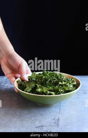 Weibliche Hand hält eine Schüssel mit gebackenen Grünkohl Chips. Stockfoto