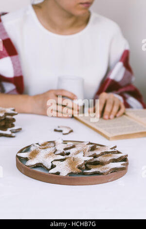 Eine Frau, die Kaffee und Schneeflocke Cookies beim Lesen eines Buches. Stockfoto