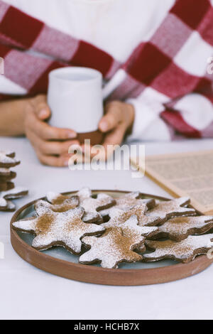 Eine Frau, die Kaffee und Schneeflocke Cookies beim Lesen eines Buches. Stockfoto