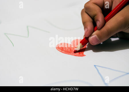 Kind, rotes Herz mit roten Farbstift auf weißem Papier zu zeichnen. Stockfoto