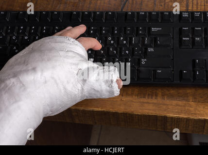 Person trägt einen Gipsarm nach der Trennung von ihrem Handgelenk Schwierigkeiten auf einer Computertastatur tippen Stockfoto