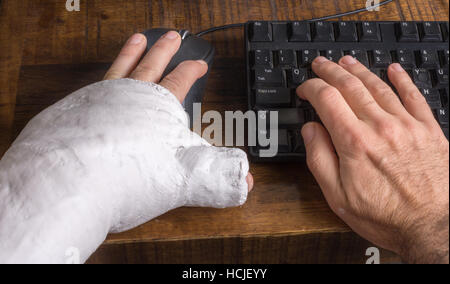 Junge Mann trägt einen Gipsarm nach der Trennung von seinem Handgelenk Schwierigkeiten mit einer Computermaus Stockfoto