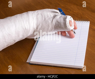 Person trägt einen Gipsarm nach der Trennung von ihrem Handgelenk versucht, einen Hinweis auf ein Stück Papier zu schreiben Stockfoto