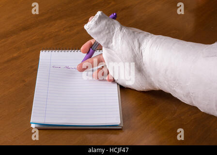 Person trägt einen Gipsarm nach der Trennung von ihrem Handgelenk versucht, einen Hinweis auf ein Stück Papier zu schreiben Stockfoto