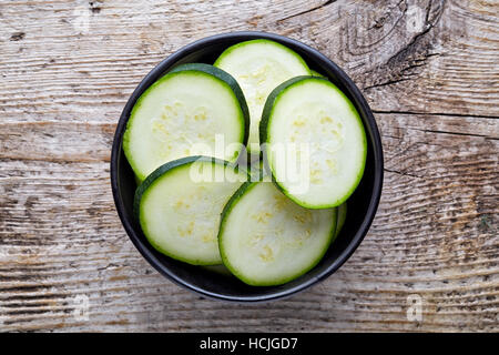 Schüssel mit frischen Zucchinischeiben auf hölzernen Hintergrund, Ansicht von oben Stockfoto