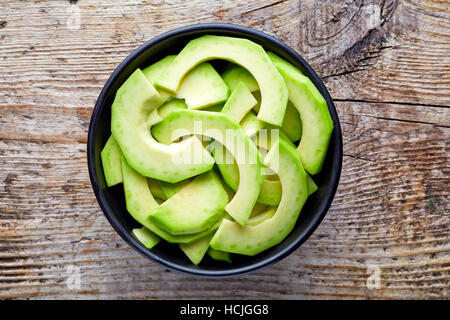 Schüssel mit Avocadoscheiben auf hölzernen Hintergrund, Ansicht von oben Stockfoto